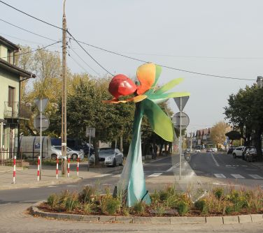 rzeźba kwiatowa na rondzie, w tle ulica po lewej i prawej drzewa, chodnik, samochody, słupy