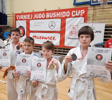 Hala sportowa. Czterech Czterech chłopców w kimonach do judo trzyma dyplomy i medale