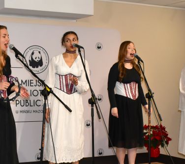 Pomiszczenie. Cztery kobiety na scenie śpiewają do mikrofonu