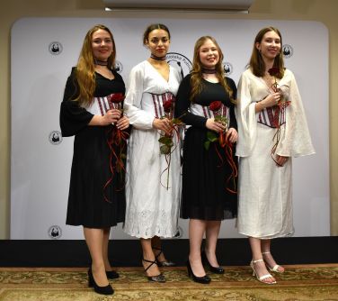 Pomieszczenie. Cztery kobiety z czerwonymi różami w rękach pozują do zdjęcia