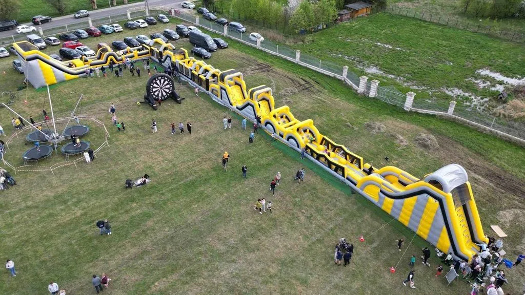Duża, żółto-szara dmuchana tor przeszkód z ludźmi bawiącymi się na łące.
