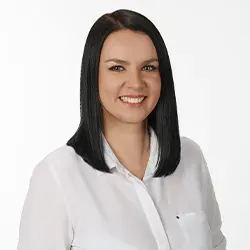 Kobieta o prostych, czarnych włosach uśmiechająca się, ubrana w białą koszulę.