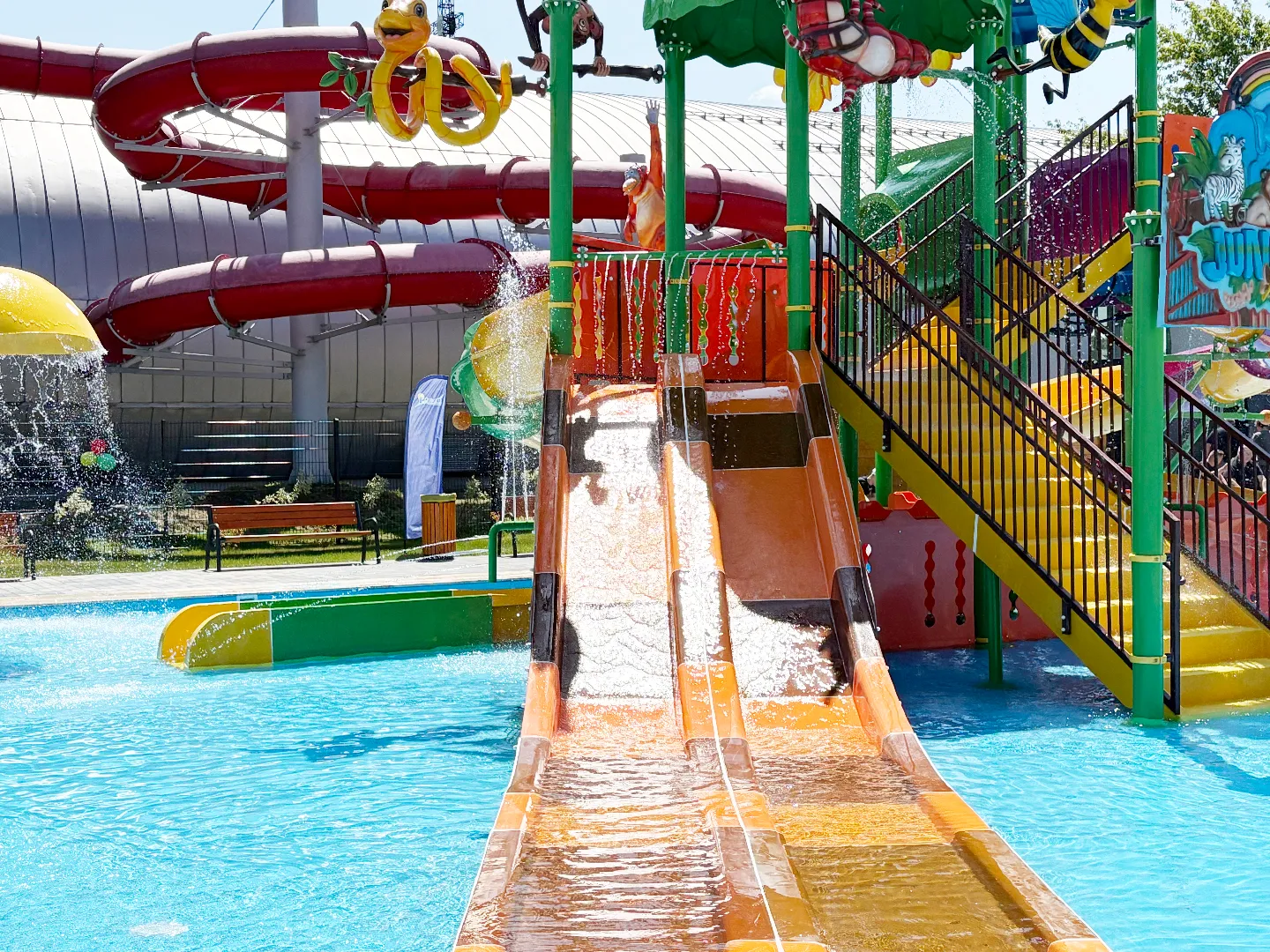 Wodne zjeżdżalnie i kolorowa konstrukcja placu zabaw z wodą oraz lejące się strumienie wody.