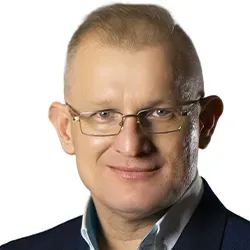 Mężczyzna w okularach, ubrany w granatową marynarkę i jasną koszulę, na białym tle.