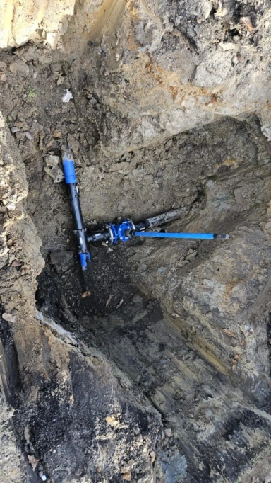 Wykopany dół z widocznym fragmentem instalacji wodociągowej z czarnych i niebieskich rur.