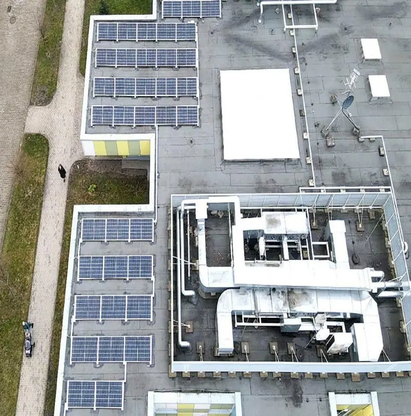 Na dachu budynku zamontowane panele słoneczne oraz instalacje wentylacyjne i rury.