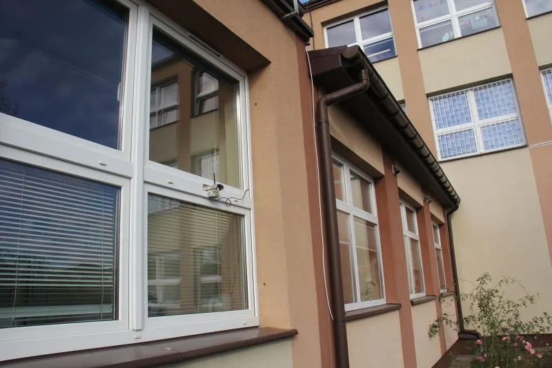 Elewacja budynku z białymi oknami i brązowymi rurami spustowymi.