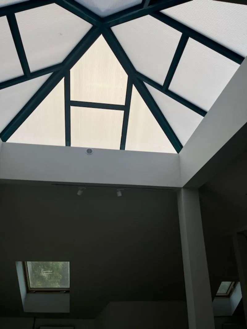 Szklany dach w formie trójkątnej konstrukcji z ramami z ciemnego metalu nad jasnym wnętrzem.