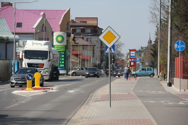 Ulica z zaparkowanymi samochodami, znaki drogowe oraz stacja paliw BP w tle.