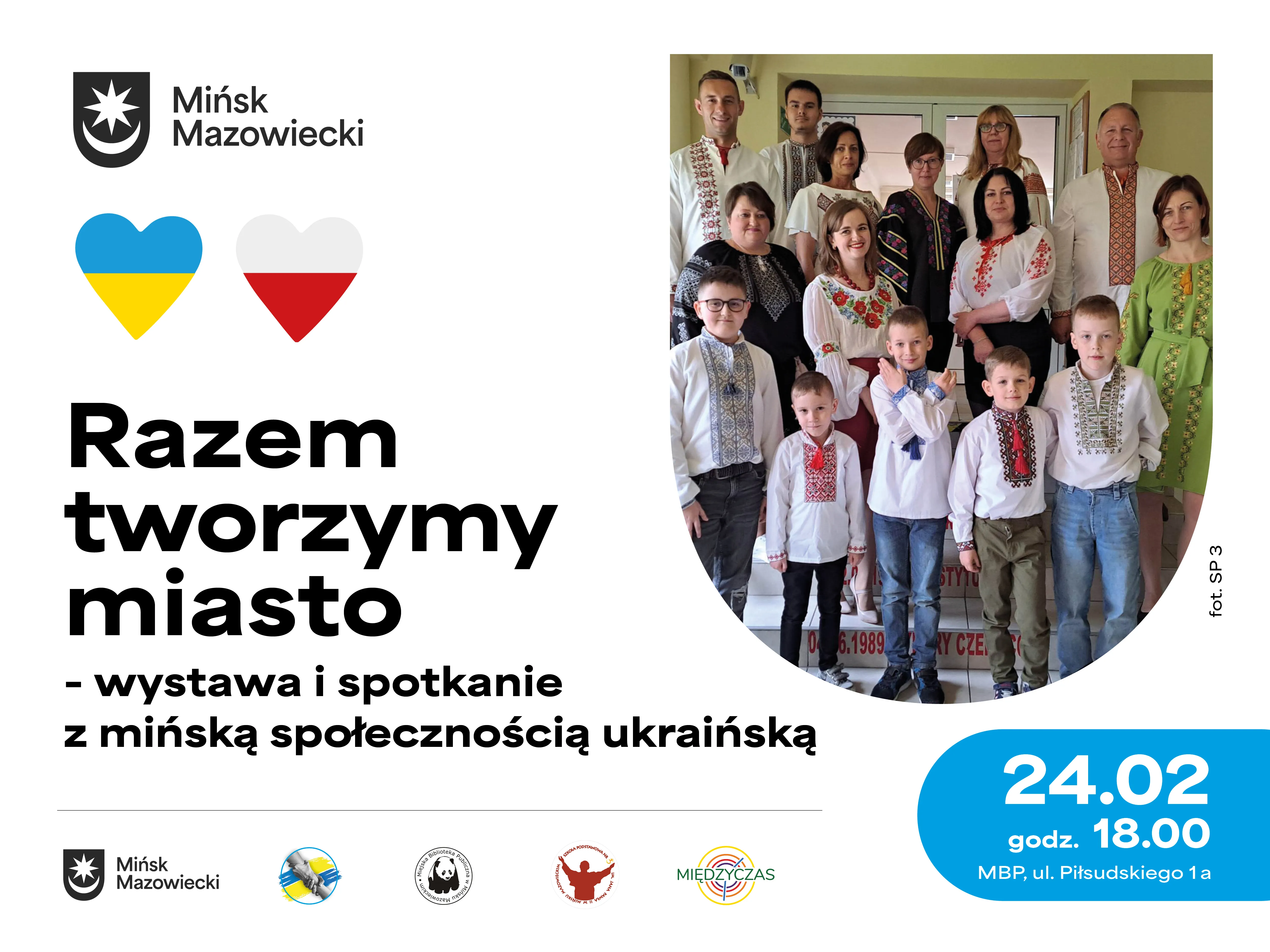 Grupa około piętnastu osób — dorośli i dzieci — ubrana w haftowane, tradycyjne stroje ukraińskie, stoi wewnątrz przy drzwiach. Po lewej jasne tło z dwoma sercami w barwach Ukrainy i Polski, kilkoma logotypami i niebieskim okrągłym panelem informacyjnym.