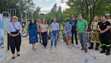 Grupa jedenastu dorosłych osób stoi na zewnątrz na placu zabaw w ciągu dnia, w tle widoczne jest wyposażenie placu oraz zieleń drzew.