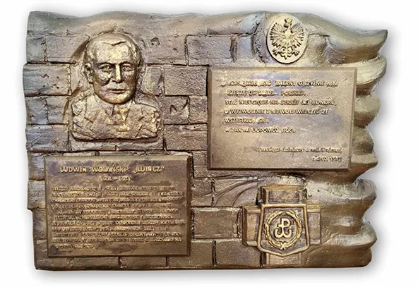 Brązowa tablica pamiątkowa z tłem stylizowanym na mury z cegieł. W górnym lewym rogu znajduje się płaskorzeźbowe popiersie mężczyzny. Po prawej u góry widoczny jest orzeł, poniżej prostokątna tablica z wygrawerowanym tekstem. W dolnej części po lewej jest większa tablica z tekstem, a po prawej tarczowy emblemat z kotwicą.