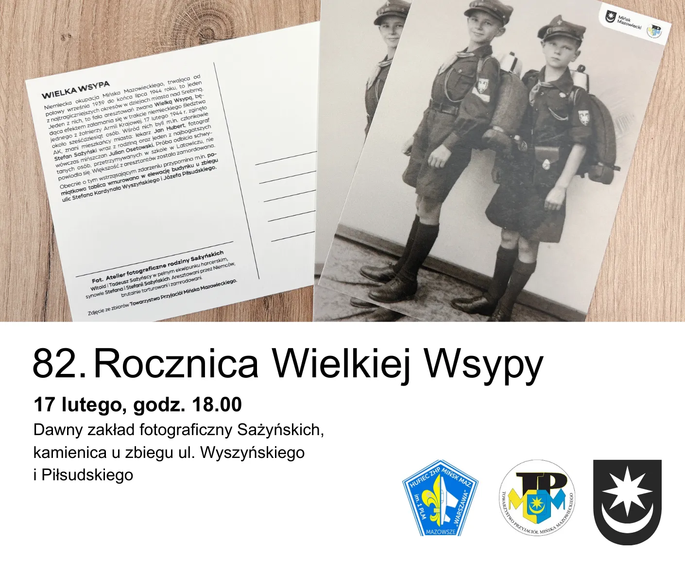 Kartka pocztowa leży na drewnianym stole, obok znajduje się czarno-białe zdjęcie dwóch chłopców w mundurkach harcerskich z plecakami. Poniżej jest tekst zapraszający na 82. rocznicę Wielkiej Wyspy z datą, godziną i miejscem wydarzenia. Po prawej stronie na dole są trzy logotypy organizatorów.