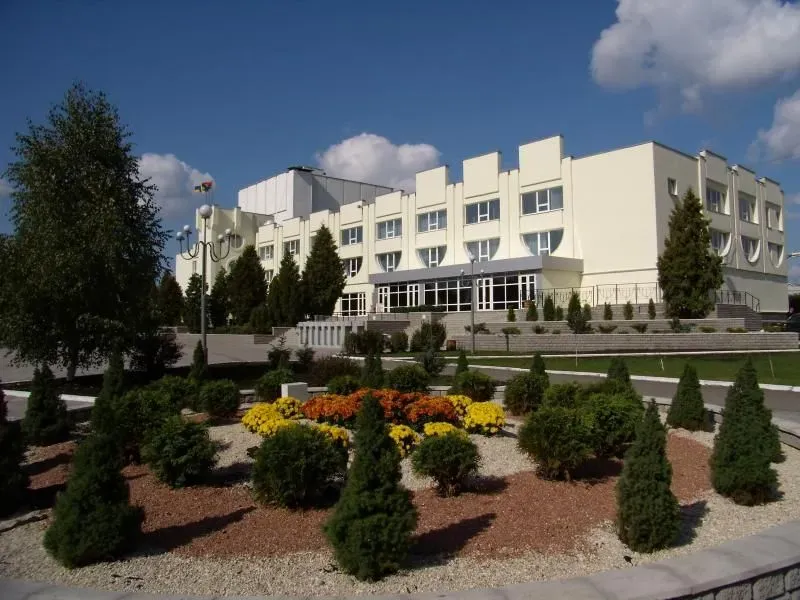 Budynek biurowy otoczony zadbaną zielenią z iglastymi krzewami i kwiatami w centrum.