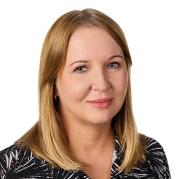 Kobieta o blond włosach, niebieskich oczach i jasnej karnacji, ubrana w czarną bluzkę w biały wzór.