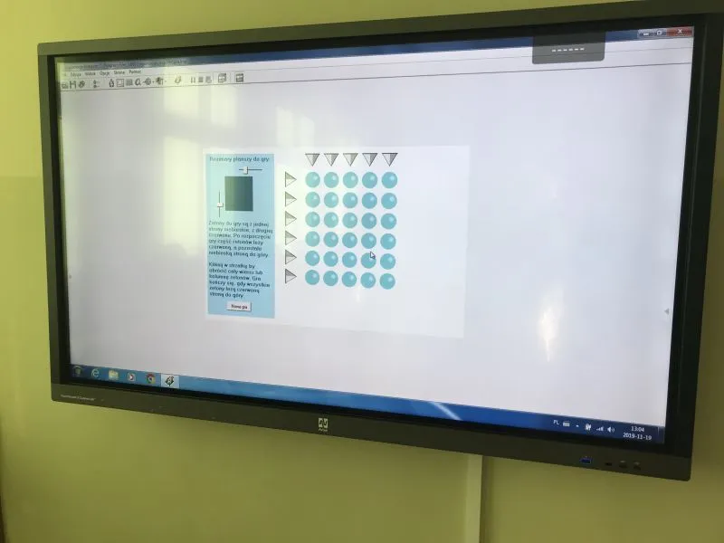 Ekran telewizora pokazujący planszę do gry z niebieskimi kółkami ułożonymi w siatkę i instrukcją po lewej stronie.