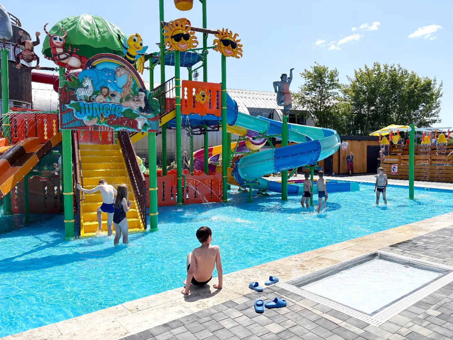 Dzieci bawiące się w kolorowym basenie z wodnym placem zabaw i zjeżdżalniami.