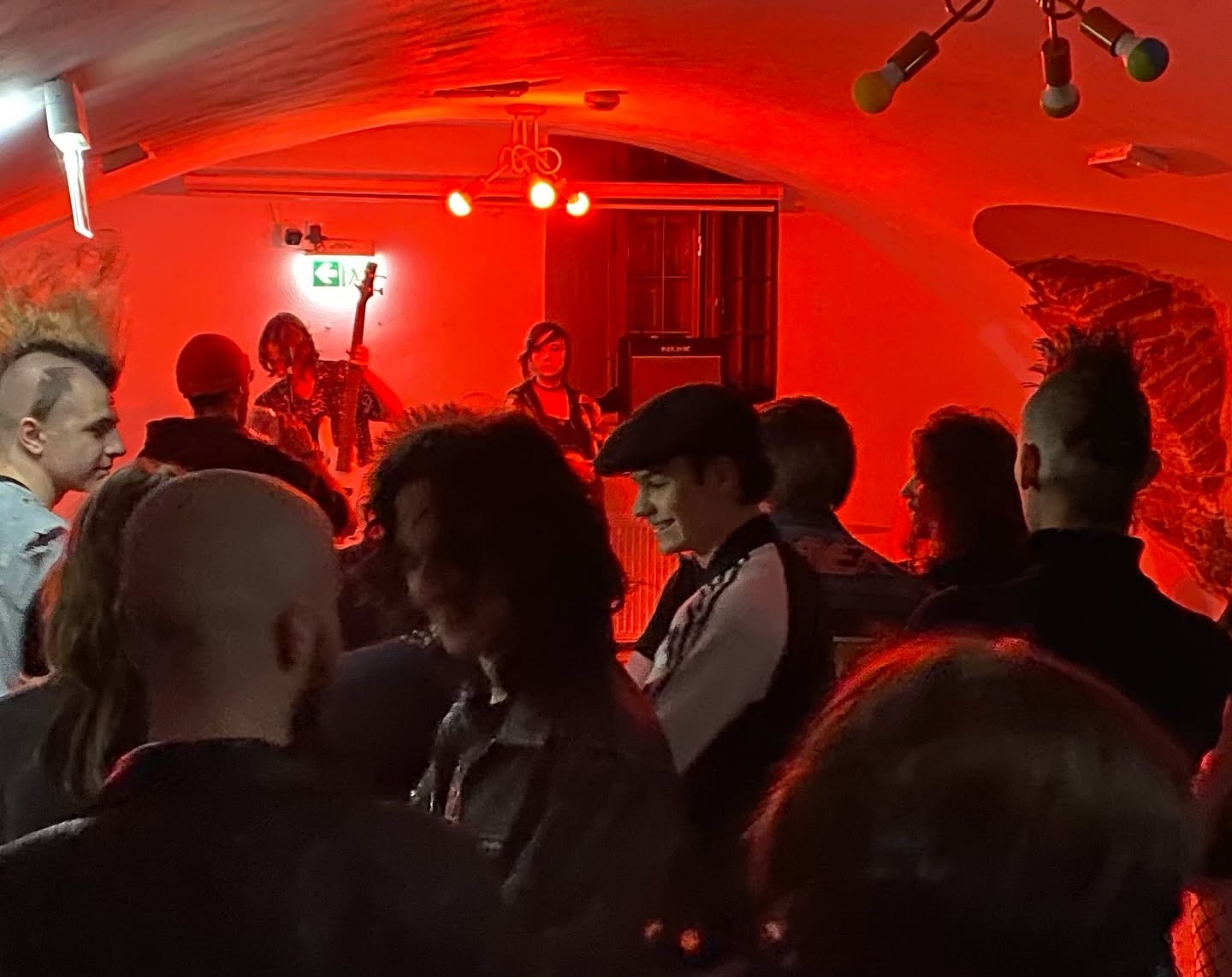 Kameralny klub o czerwonym oświetleniu. Na scenie dwie osoby grają na gitarach. Przed sceną stoi tłum ludzi. W tłumie widać kilka osób z irokezami i z czapkami. Niskie, sklepione wnętrze z sufitowymi lampami.