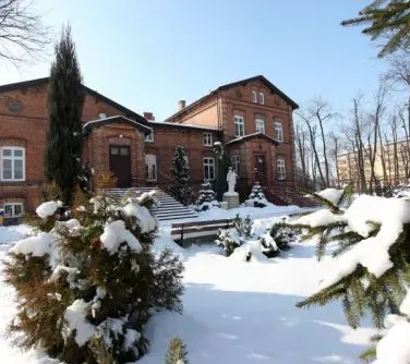 Budynek z czerwonej cegły w zimowym otoczeniu z pokrytymi śniegiem krzewami i drzewami.