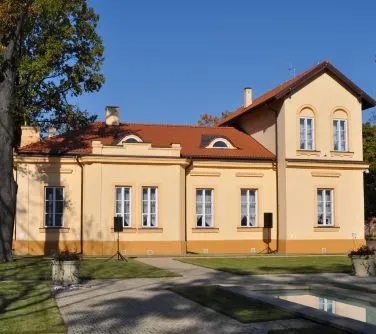 Budynek mieszkalny o kremowych ścianach, czerwonym dachu i kilku oknach z białymi ramami oraz drzwiami.