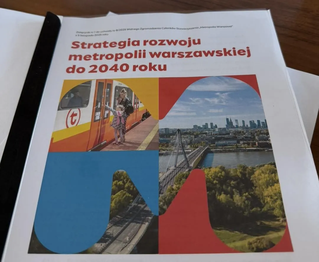 Kliknięcie powiększy obraz. Dokument leżący na drewnianym stole z tytułem „Strategia rozwoju metropolii warszawskiej do 2040 roku” oraz kolorowymi zdjęciami: dziecko wsiadające do tramwaju, panorama Warszawy z mostem i zielonym terenem.