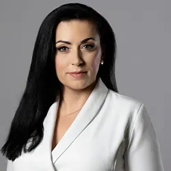 Kobieta z długimi czarnymi włosami w białej marynarce na szarym tle.