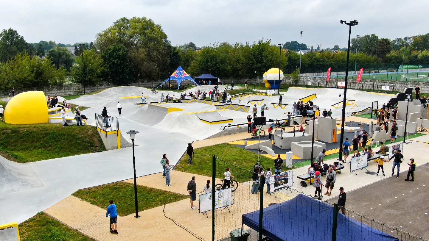 Miejski skatepark z rampami, przeszkodami i wieloma osobami jeżdżącymi na rowerach, deskorolkach i hulajnogach.