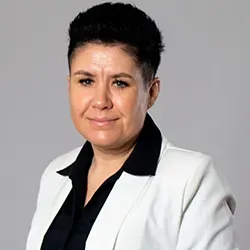 Kobieta w białej marynarce i czarnej koszuli na szarym tle.