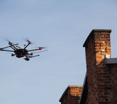 Po lewej dron na tle nieba. Po prawej stary kamienny komin budynku