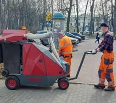 Pracownicy ZGK  sprzatają chodnik w okolicy parku używając nowego urządzenia, przypominającego dużych rozmiarów odkurzacz.
