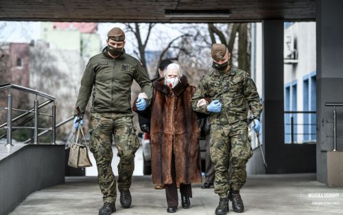 Dwaj terytorialsi pomagają starszej osobie w drodze do punktu szczepień.