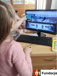 dziewczynka ćwiczy przy monitorze komputerowym, ktoś wskazuje palcem na monitorze