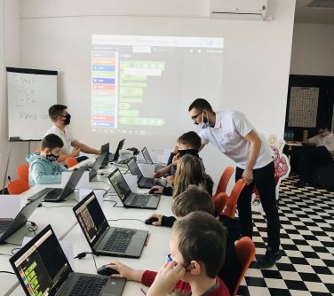 Grupa dzieci z instruktorem kodują w komputerach.
