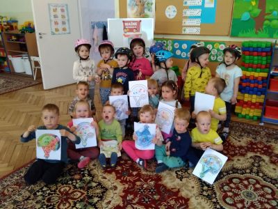 Wnętrze przedszkola. Na dywanie dzieci pozują z kartaki  dłonaich