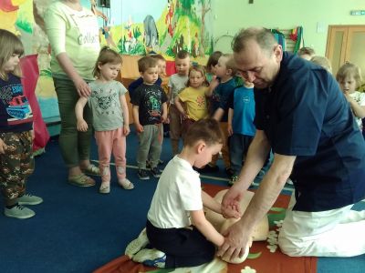 Wnętrze przedszkola. Na dywanie dzieci oraz mężczyzna klęczy. obok niego dziecko