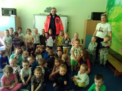 Wnętrze przedszkola. Grupa dzieci . Za nimi ratownik