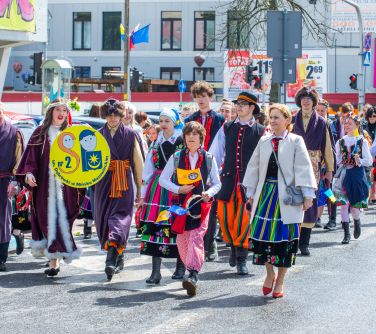 Dzień, słońce. Ulicą maszerują osoby w przebraniach. Przed soba duże koło z logo szkoły
