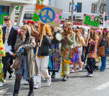 Dzień, słońce. Po ulicy maszerują osoby w przebraniach hipisowskich