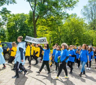 Słoneczny dizeń. Po alejce maszerują osoby przebrane w żółte i niebieskie koszulki