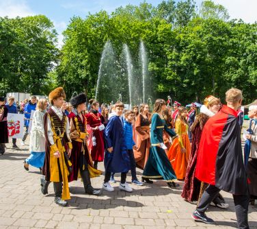 Słoneczny dzień. Osoby w przebraniach maszerują na tle fontanny