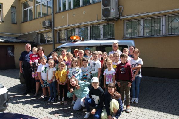 zdjęcie grupowe dzieci i opiekunów z Klubu Przełom, po obydwu stronach strażnicy miejscy. Zdjecie na tle samochodu Straży...