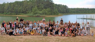 Zdjęcie grupowe uczestników obozu sportowego. Grupa stoi na terenie zielonym, w tle jezioro