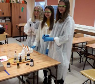 uśmiechnięte dziewczęta w fartuchach podczas zajęć chemicznych