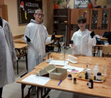 uśmiechnięci chłopcy w fartuchach podczas zajęć chemicznych