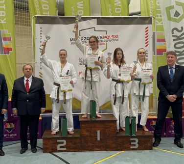 zawodniczki karate stoją na podium w towarzystwie mężczyzn w garniturach