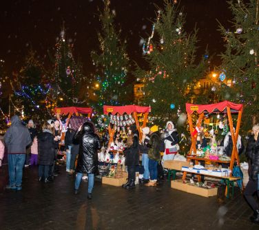 osoby na placu przy stojakach drewnianych oglądają rzeczy