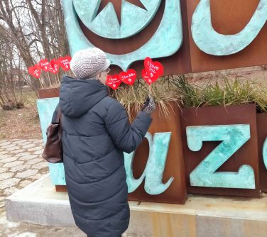kobieta stoi tyłem do napisu Mińsk Mazowiecki, trzyma w reku serce czerwone na patyku