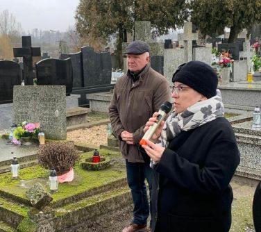miezy grobami kobieta przemawia do mikrofonu, obok stoi mężczyzna