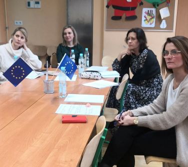 kobiety siedzą przy ławkach szkolnych, na ławce wazon z dwiema flagami UE