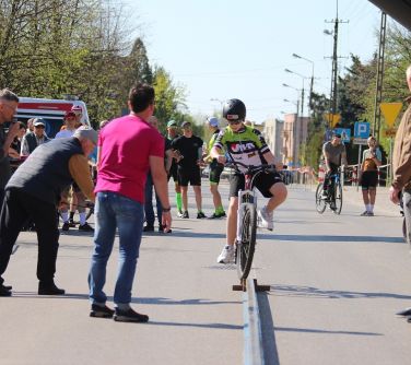 chłopiec na rowerze jedzie po szynie, naokoło osoby stojące na ulicy